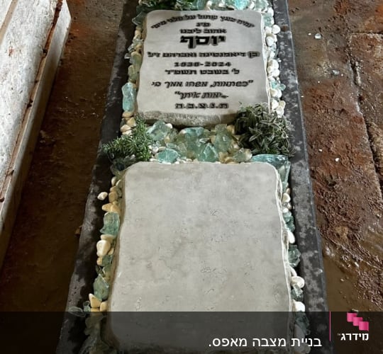 מצבה עם כיתוב בעברית, אבנים ירוקות וצמחייה מסביב